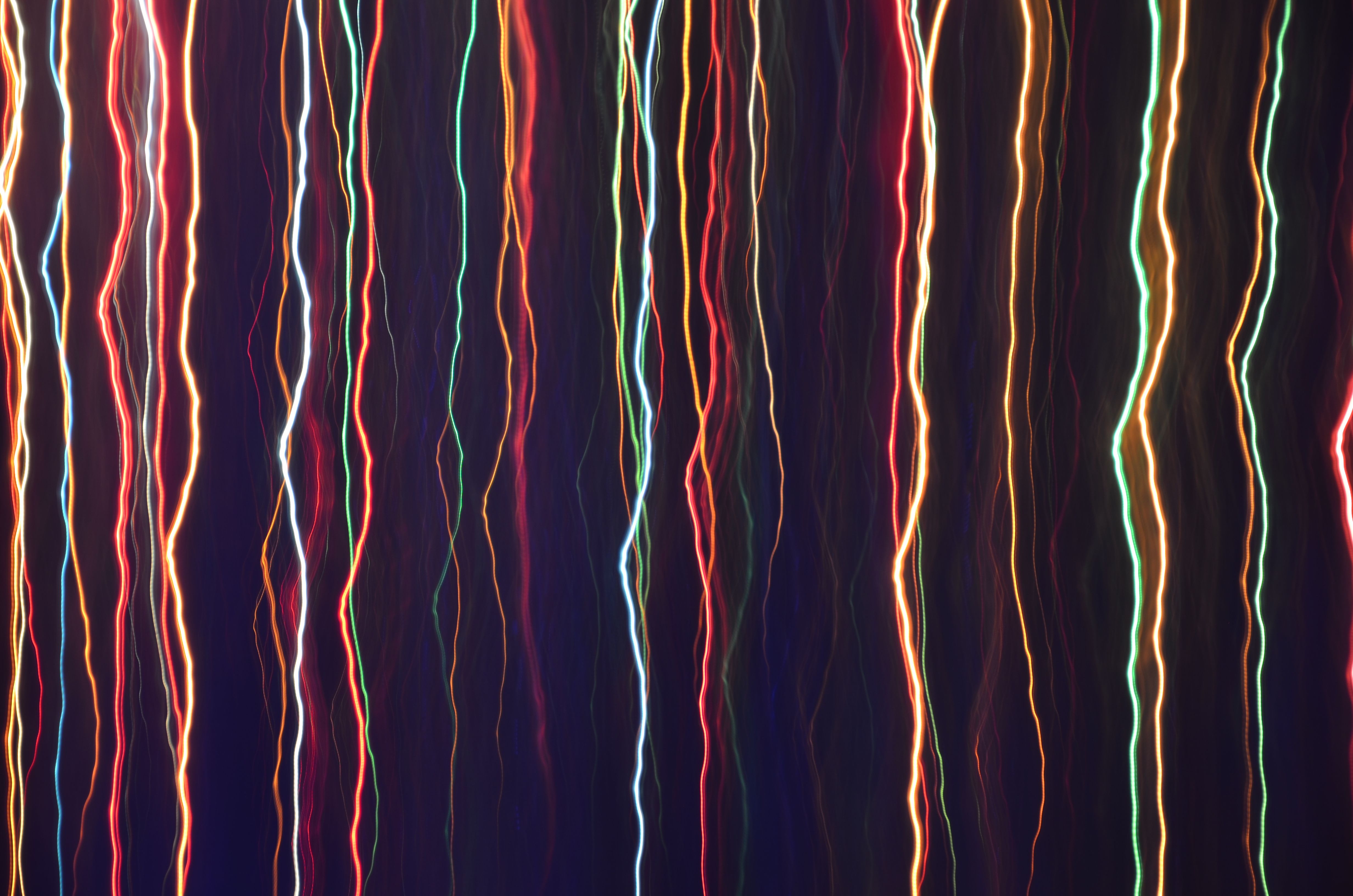 Fine threads of coloured light falling like rain on black.